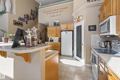 Kitchen featuring solid wood cabinetry, a built-in microwave, white tile backsplash, and a glass-paneled pantry door - 21 Pipestone Drive, Devon, AB - Indoor Photo Showing Kitchen