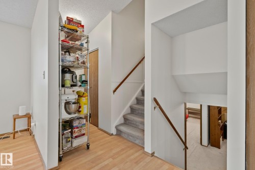 Split-level entry featuring wood-finish flooring, a carpeted staircase with a wood handrail, and white walls - 4707 10A Avenue, Edmonton, AB 