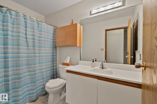 Bathroom featuring a white vanity with integrated sink, chrome faucet, wall-mounted mirror, overhead light fixture, and wood-finish cabinetry - 4707 10A Avenue, Edmonton, AB 