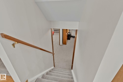 Carpeted staircase with light-colored walls and a wood handrail - 4707 10A Avenue, Edmonton, AB 