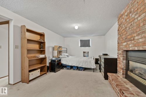 Carpeted room featuring a brick fireplace with a raised hearth, a built-in wood bookshelf, and a ceiling light fixture - 4707 10A Avenue, Edmonton, AB 