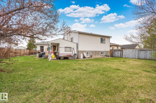Expansive grassy backyard featuring a partial wood fence, mature tree, and a covered patio area with a white siding exterior - 4707 10A Avenue, Edmonton, AB 