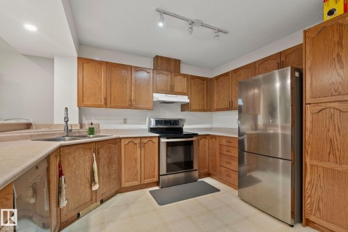 Corner kitchen featuring wood cabinetry, stainless steel appliances, light-toned countertops, and track lighting - 4707 10A Avenue, Edmonton, AB 