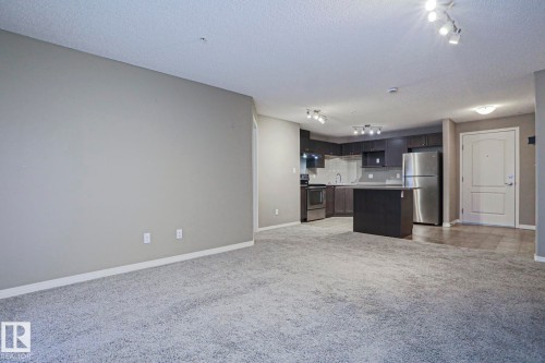 Open-concept living area featuring light gray carpeting and a contemporary kitchen - 201 1520 Hammond Gate Gate, Edmonton, AB 