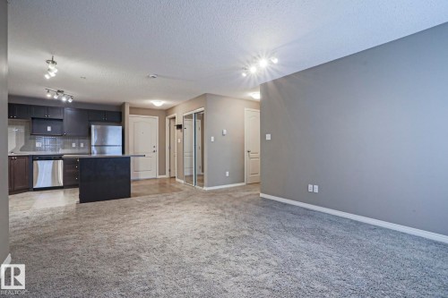 Open-concept living space featuring a kitchen with dark cabinetry, stainless steel appliances, a tiled backsplash, and an island - 201 1520 Hammond Gate Gate, Edmonton, AB 