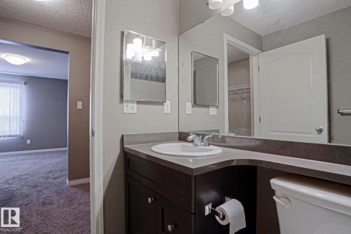 Bathroom vanity with an integrated sink, dark wood-finish cabinetry, and a full-width mirror - 201 1520 Hammond Gate Gate, Edmonton, AB 