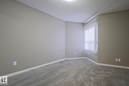 Carpeted room with a window featuring vertical blinds, neutral wall paint, and white baseboards - 201 1520 Hammond Gate Gate, Edmonton, AB 