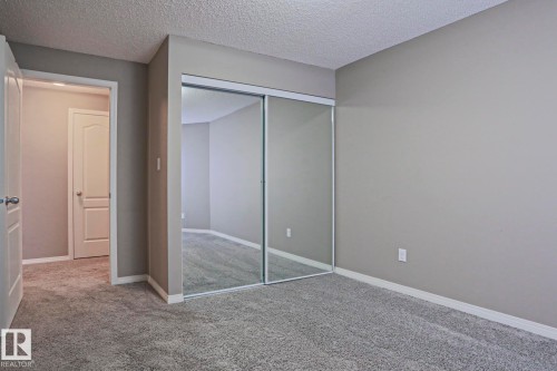 Plush gray carpeting and neutral wall tones define this room, featuring a mirrored closet with sliding doors - 201 1520 Hammond Gate Gate, Edmonton, AB 