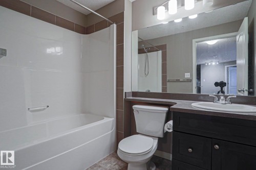 Bathroom featuring a white bathtub with shower, a vanity with a white oval sink, and a large mirror - 201 1520 Hammond Gate Gate, Edmonton, AB 