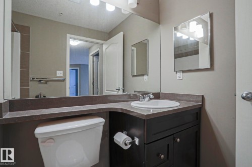 Bathroom featuring a vanity with an integrated sink, dark wood cabinetry, a large wall mirror, and a toilet - 201 1520 Hammond Gate Gate, Edmonton, AB 