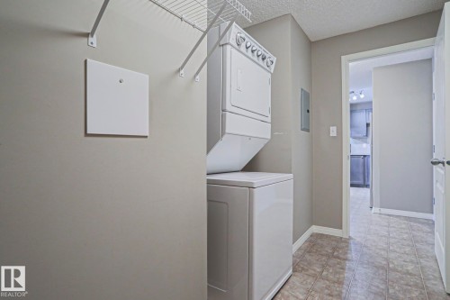 Laundry area featuring a stacked washer and dryer, tile flooring, and overhead wire shelving - 201 1520 Hammond Gate Gate, Edmonton, AB 