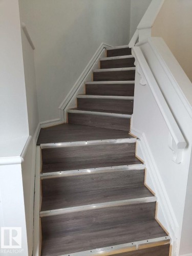 The property features a staircase with dark wood-look treads, white risers, and a white handrail - 115 Keystone Lane, Leduc, AB - Indoor Photo Showing Other Room