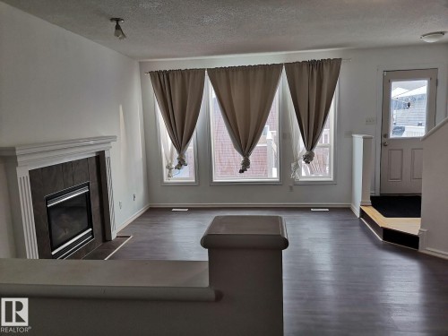 This property features dark wood-look flooring and a fireplace with a white mantel and dark tile surround - 115 Keystone Lane, Leduc, AB - Indoor Photo Showing Living Room With Fireplace