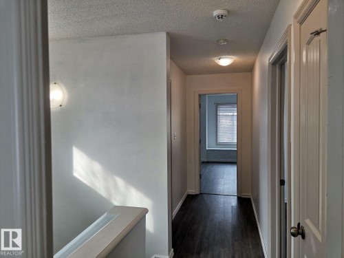 Well-lit hallway with dark wood flooring, white walls, and a ceiling light fixture - 115 Keystone Lane, Leduc, AB - Indoor Photo Showing Other Room
