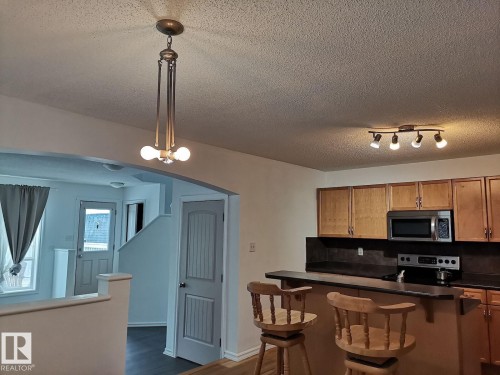 The kitchen features wood cabinetry, a stainless steel microwave, and a black electric range with a matching backsplash - 115 Keystone Lane, Leduc, AB - Indoor Photo Showing Kitchen