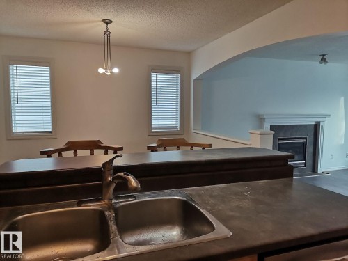 Kitchen area featuring a double basin sink with a chrome faucet, a breakfast bar, and an arched entryway leading to a living space with a fireplace - 115 Keystone Lane, Leduc, AB - Indoor Photo Showing Kitchen With Double Sink