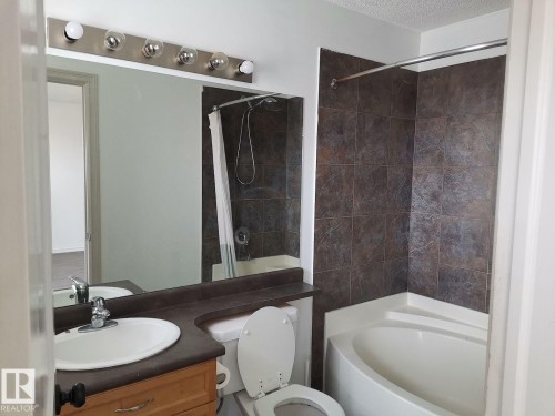 Bathroom featuring a vanity with a white basin and chrome faucet, a large mirror, and a bathtub with dark tiled walls - 115 Keystone Lane, Leduc, AB - Indoor Photo Showing Bathroom