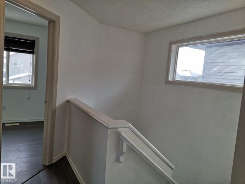 The property features a staircase with a white wooden handrail and a window with blinds providing natural light - 115 Keystone Lane, Leduc, AB - Indoor Photo Showing Other Room