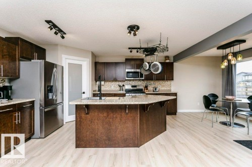 Kitchen featuring wood-finish flooring, dark wood cabinetry, stainless steel appliances, a center island with a light-toned countertop, and a decorative pendant light fixture above the dining area - 42 Santana Crescent, Fort Saskatchewan, AB - Indoor Photo Showing Kitchen