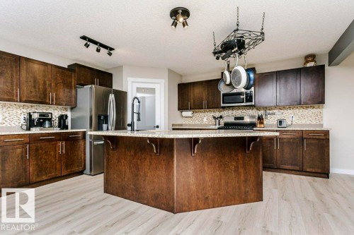 Kitchen featuring dark wood-finish cabinetry, light-toned countertops, stainless steel appliances, and a central island with an integrated sink - 42 Santana Crescent, Fort Saskatchewan, AB - Indoor Photo Showing Kitchen With Upgraded Kitchen