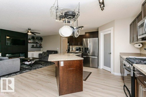 Open-concept living space featuring wood-finish flooring, a kitchen island with stone-finish countertop, dark wood cabinetry, and stainless steel appliances - 42 Santana Crescent, Fort Saskatchewan, AB - Indoor Photo Showing Kitchen With Stainless Steel Kitchen With Upgraded Kitchen