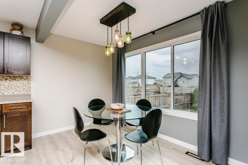 Open dining area featuring light wood-finish flooring, a contemporary chandelier, a window wall, and dark brown cabinetry with a tiled backsplash - 42 Santana Crescent, Fort Saskatchewan, AB - Indoor Photo Showing Dining Room