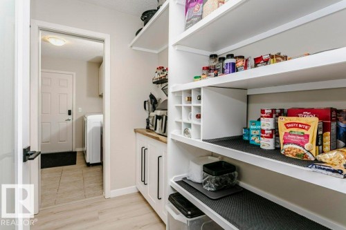 Pantry featuring extensive built-in shelving, integrated wine storage, lower cabinetry with black hardware, and wood-finish flooring - 42 Santana Crescent, Fort Saskatchewan, AB - Indoor Photo Showing Other Room