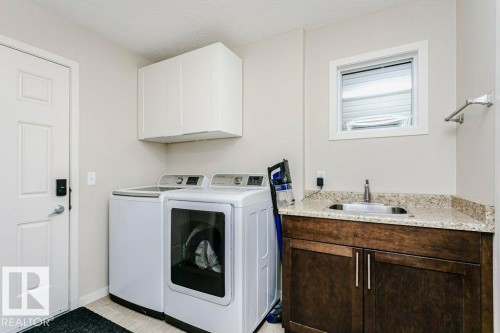 Utility room featuring a built-in sink with a granite-look countertop, dark wood-finish cabinetry, and overhead white storage cabinets - 42 Santana Crescent, Fort Saskatchewan, AB - Indoor Photo Showing Laundry Room