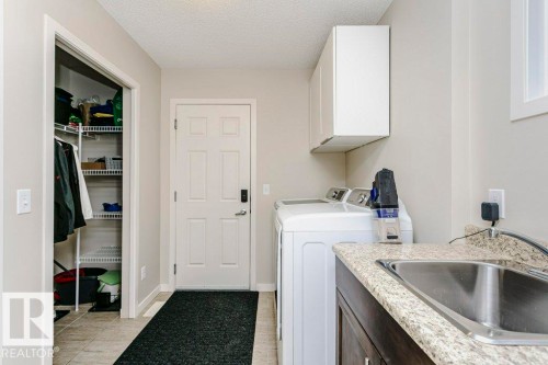 Utility area featuring a laundry sink with a granite-style countertop, white upper cabinetry, and a storage closet with wire shelving - 42 Santana Crescent, Fort Saskatchewan, AB - Indoor Photo Showing Laundry Room