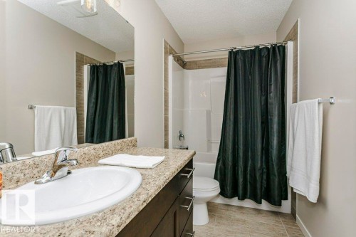 Bathroom featuring a white porcelain drop-in sink, speckled countertop, dark wood-finish cabinetry, and a shower-tub combination with light-toned tiled surround - 42 Santana Crescent, Fort Saskatchewan, AB - Indoor Photo Showing Bathroom