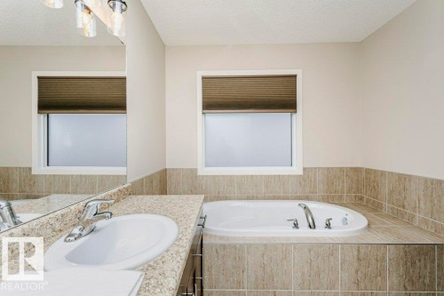 Bathroom featuring an integrated oval soaking tub with deck-mounted fixtures, and a vanity with a drop-in sink and stone-finish countertop - 42 Santana Crescent, Fort Saskatchewan, AB - Indoor Photo Showing Bathroom