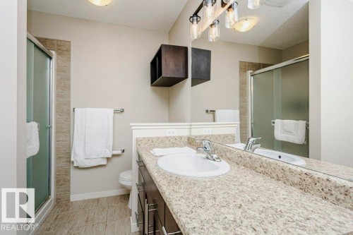 Bathroom featuring a granite-finish countertop, wood-finish vanity with chrome hardware, walk-in shower with tiled surround, and tiled flooring - 42 Santana Crescent, Fort Saskatchewan, AB - Indoor Photo Showing Bathroom