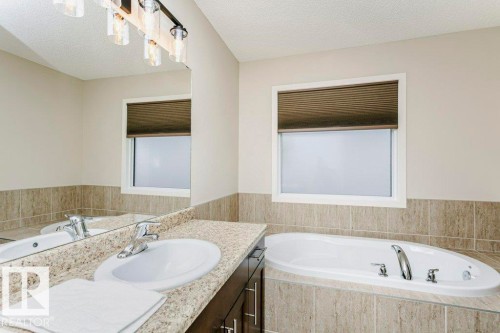 Bathroom featuring a built-in soaking tub, a single vanity with a granite-style countertop, and a large mirror - 42 Santana Crescent, Fort Saskatchewan, AB - Indoor Photo Showing Bathroom
