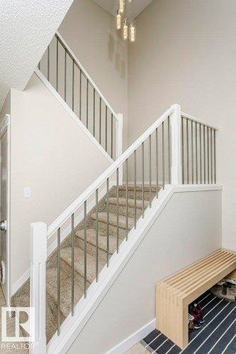 Two-story entry featuring a contemporary chandelier and carpeted stairs with white risers and dark balusters - 42 Santana Crescent, Fort Saskatchewan, AB - Indoor Photo Showing Other Room
