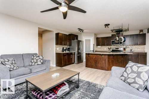 Open-concept living space featuring wood-finish flooring, a ceiling fan, dark wood cabinetry, a tiled backsplash, and stainless steel appliances - 42 Santana Crescent, Fort Saskatchewan, AB - Indoor