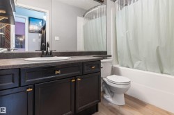 Bathroom featuring a black vanity with gold hardware, integrated sink, and dark countertop - 