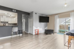 Open-concept living area with light wood-finish flooring, a kitchen pass-through with a breakfast bar, and a sliding glass door leading to a patio - 