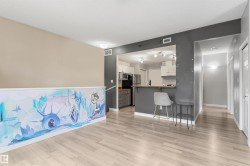 Contemporary open-concept living space featuring wood-finish flooring, a kitchen pass-through with breakfast bar, track lighting, and a neutral color palette - 