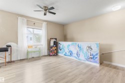 Bright room featuring wood-finish flooring, a contemporary ceiling fan, and a large window with white curtain panels - 