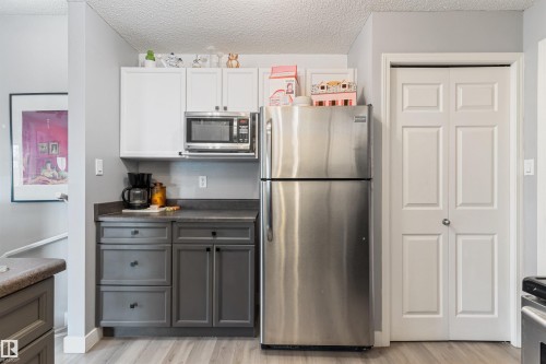 Kitchen area featuring stainless steel appliances, two-tone cabinetry with white upper and gray lower cabinets, dark countertop, and wood-finish flooring - 73 3040 Spence Wynd, Edmonton, AB - Indoor Photo Showing Kitchen With Stainless Steel Kitchen