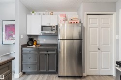 Kitchen area featuring stainless steel appliances, two-tone cabinetry with white upper and gray lower cabinets, dark countertop, and wood-finish flooring - 