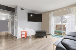 Spacious living area featuring light wood-finish flooring, a vaulted ceiling, and a sliding glass door leading to an outdoor patio - 