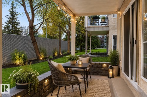 Covered outdoor patio featuring string lighting, a concrete floor, and a retaining wall - 104 9760 174 Street, Edmonton, AB - Outdoor With Deck Patio Veranda With Exterior