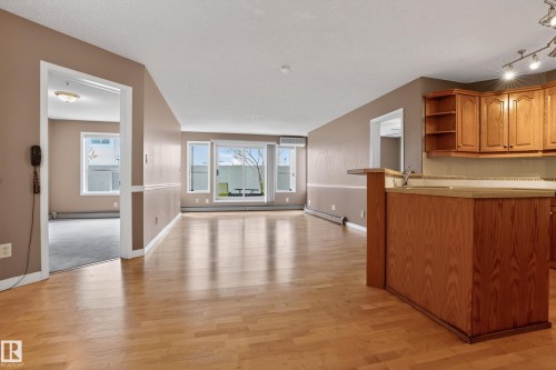 Open-concept living space featuring wood-finish flooring, a kitchen island with integrated sink, and abundant natural light from multiple windows - 104 9760 174 Street, Edmonton, AB - Indoor Photo Showing Other Room
