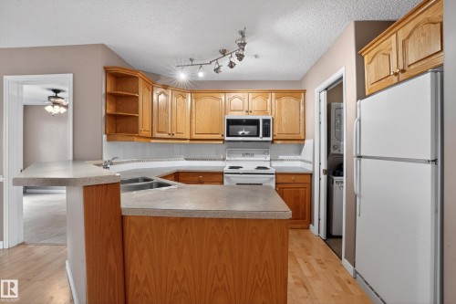 Kitchen featuring wood-finish cabinetry, an integrated breakfast bar, and laminate countertops - 104 9760 174 Street, Edmonton, AB - Indoor Photo Showing Kitchen With Double Sink