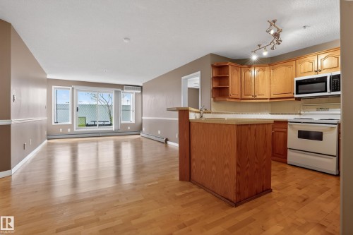 Open-concept living area featuring wood-finish flooring, a kitchen with wood cabinetry and track lighting, and expansive windows - 104 9760 174 Street, Edmonton, AB - Indoor Photo Showing Kitchen