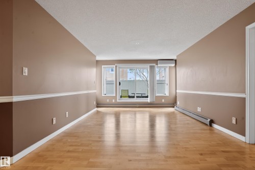 Spacious room featuring wood-finish flooring, neutral-toned walls with chair rail molding, and a sliding glass door leading to an outdoor space - 104 9760 174 Street, Edmonton, AB - Indoor Photo Showing Other Room