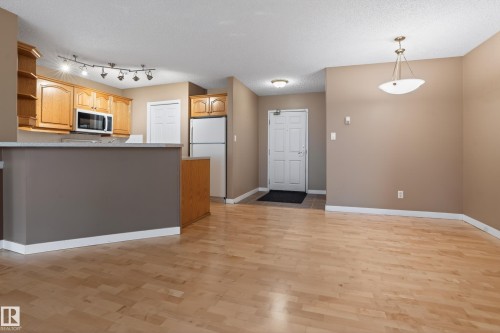 Open-concept living space featuring wood-finish flooring, a kitchen with light wood cabinetry, a built-in microwave, and track lighting - 104 9760 174 Street, Edmonton, AB - Indoor Photo Showing Kitchen