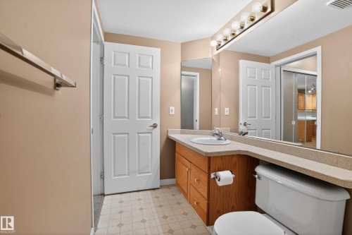 Bathroom featuring a light-toned countertop, integrated sink, and wood-finish vanity cabinetry - 104 9760 174 Street, Edmonton, AB - Indoor Photo Showing Bathroom
