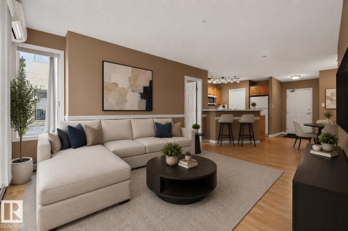 Open-concept living area featuring light wood-finish flooring, a breakfast bar with built-in cabinetry, an integrated kitchen space with track lighting, and a window with a white frame - 104 9760 174 Street, Edmonton, AB - Indoor Photo Showing Living Room